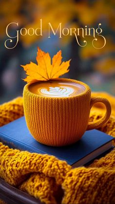 a cup of coffee sitting on top of a book next to a yellow sweater and maple leaf