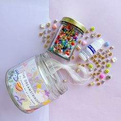 a jar filled with lots of colorful beads next to other items on a pink surface