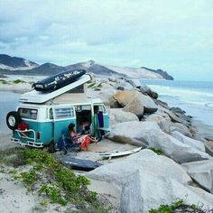 an old vw camper van parked on the beach next to some rocks and surfboards