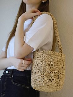 a woman is holding a crocheted handbag in her right hand and wearing a white t - shirt