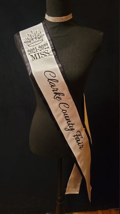 a black mannequin with a white sash on it's head and some writing on the ribbon