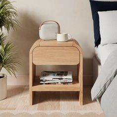 a nightstand with magazines and a cup on it next to a bed in a bedroom