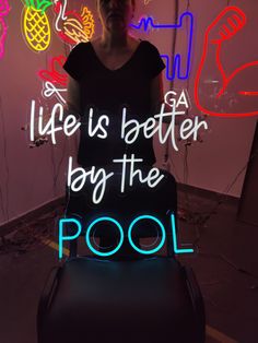 a woman standing in front of a neon sign that says life is better by the pool