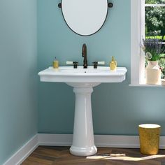 a white pedestal sink sitting under a round mirror in a blue bathroom with wooden floors