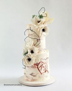 a wedding cake with white flowers on top and red writing on the bottom that says love