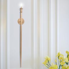 a vase with yellow flowers sitting next to a wall mounted clock on a white wall