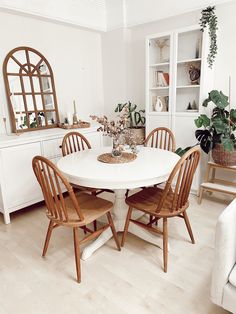 a white table with four chairs around it in a room filled with plants and other furniture