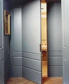 an open door leading into a bathroom with wood floors and gray walls, in front of a sink