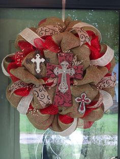 a wreath with a cross on it hanging from the front door, decorated with burlocks and ribbons