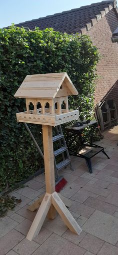 a wooden bird house sitting on top of a table next to a ladder and bushes