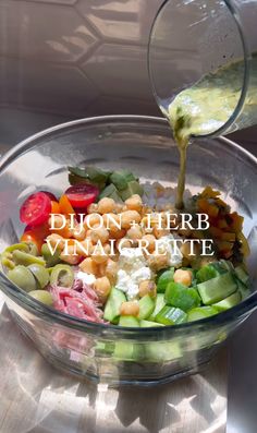 a person pouring dressing into a glass bowl filled with vegetables and cucumber slices