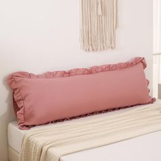 a bed with a pink pillow on top of it next to a white wall and window