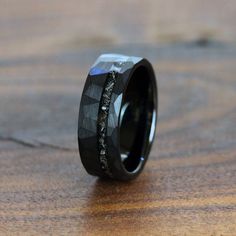 a wedding band with black diamond inlays is shown on a wooden surface and looks like it has been made out of wood