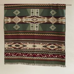 a blanket hanging on a clothes line with a white wall in the background and a red, green, and brown pattern