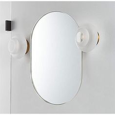 an oval mirror mounted to the side of a white wall next to a light fixture