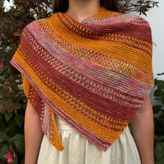 a woman standing in front of a bush wearing a yellow and red striped shawl