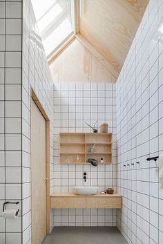 a white tiled bathroom with wooden shelves and a sink in the center, along with a skylight