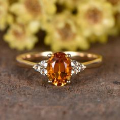 an orange and white diamond ring sitting on top of a stone surface with flowers in the background