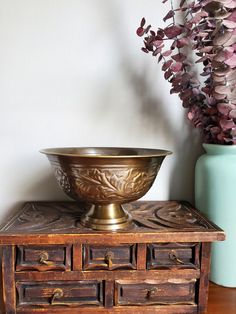 a bowl sitting on top of a wooden table next to a vase with purple flowers