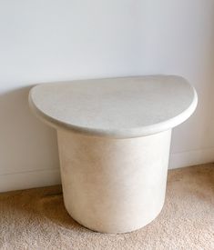 a white round table sitting on top of a carpeted floor next to a wall