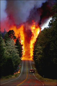 a large fire is burning on the side of a road with cars driving down it