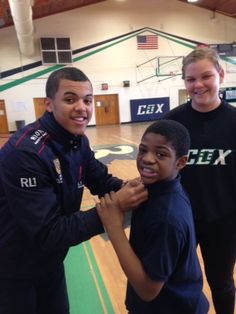 three people standing in a gym posing for a photo with a young boy who is holding his arm around another man's neck