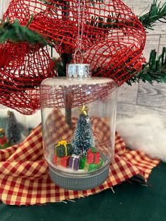 a christmas ornament in a glass jar with trees inside and presents under it