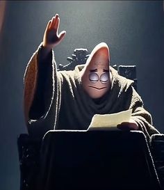 a cartoon character sitting at a desk with a book in front of him and his hands up