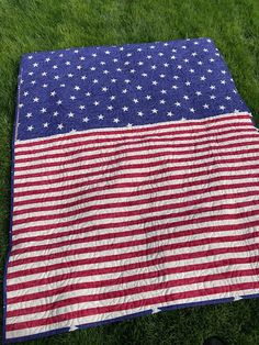 an american flag quilt is laying on the grass in front of someone's feet