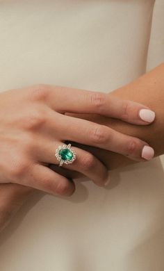 a woman's hand wearing a ring with an emerald center and diamond accents on it