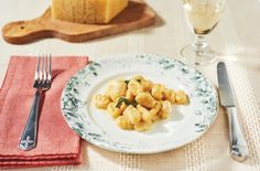 a white plate topped with ravioli next to a glass of wine and silverware