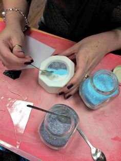 a woman is making some blue glitter in her crafting supplies on a pink table