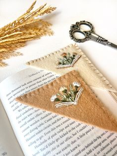 an open book with some flowers on it next to a pair of scissors and thread