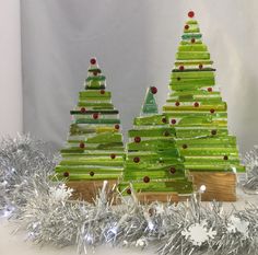 three small green christmas trees sitting on top of tinsel covered wood planks in front of silver tinsel