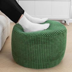 a person in white socks and black pants sitting on a green ottoman