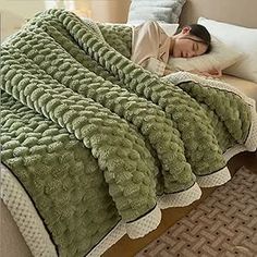 a woman laying on top of a bed under a green blanket