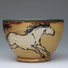 a brown and black bowl with a white horse on it's side in front of a gray background