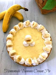 a banana cream pie sitting on top of a table next to two bananas and a basket