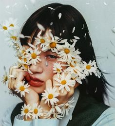 a woman with daisies on her face and hands in front of her face, surrounded by petals