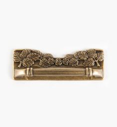 an antique brass drawer pull with roses and leaves on the front, against a white background