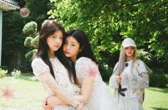 two young women standing next to each other in front of a tree and grass covered yard