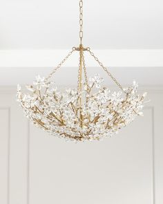 a chandelier hanging from the ceiling with white flowers on it and gold chains