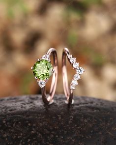 two wedding rings with green and white diamonds on top of a rock in the woods