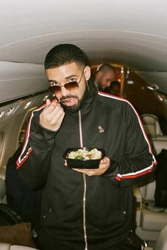 a man eating food in an airplane with sunglasses on his face and looking at the camera