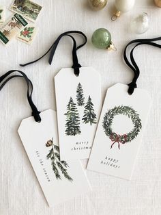 three tags with christmas trees on them are sitting next to ornaments and other items that have been placed around