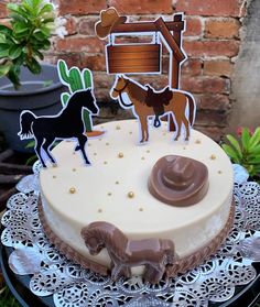 a cake decorated with horses and a cowboy hat on top of a table in front of a brick wall