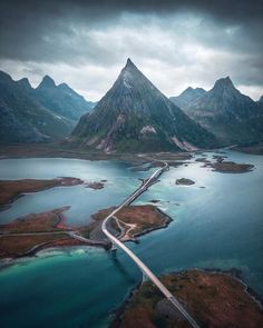 an aerial view of a road running through the water and mountains in the back ground