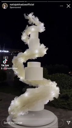 a three tiered white wedding cake sitting on top of a pedestal in front of a building