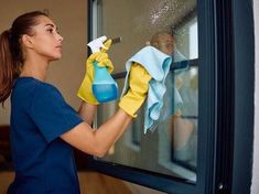 a woman in blue shirt and yellow gloves cleaning window with sprayer on it's side