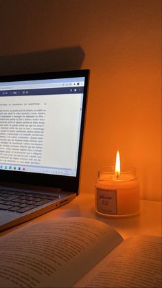 an open laptop computer sitting on top of a desk next to a candle and book